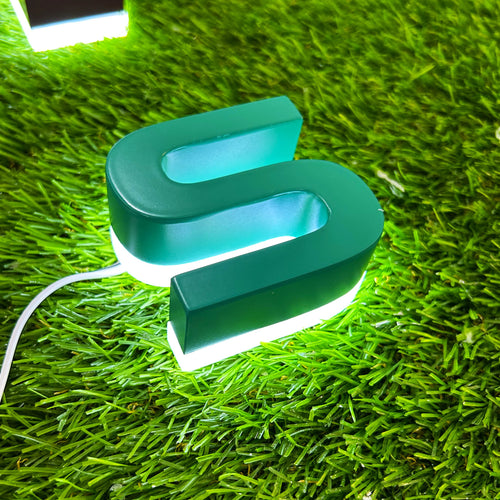 3D backlit channel letter S in teal with white LED halo on grass